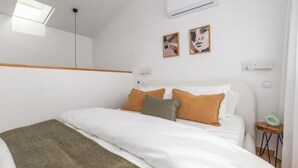 A bedroom with a bed, a skylight, an air conditioner, and two framed pictures on the wall. - URBAN LOFT PORTO (Porto)
