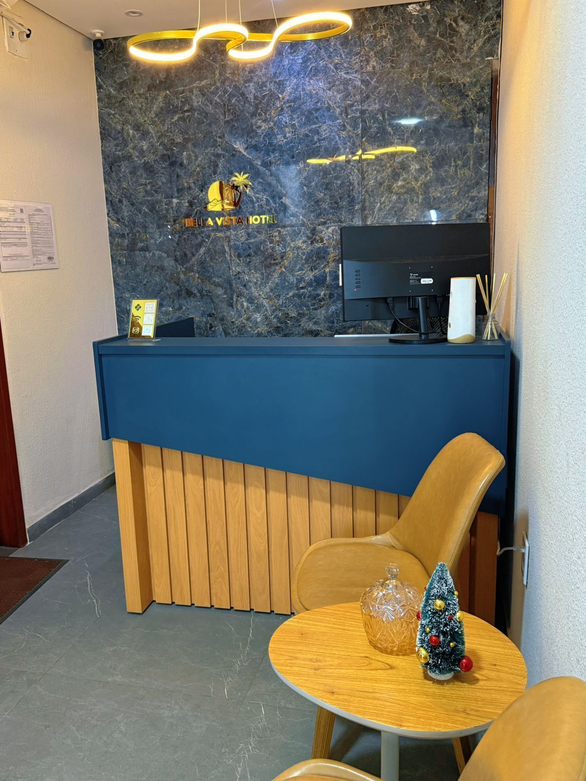 Un comptoir d’accueil d’hôtel avec un mur en marbre, un ordinateur et un petit sapin de Noël.