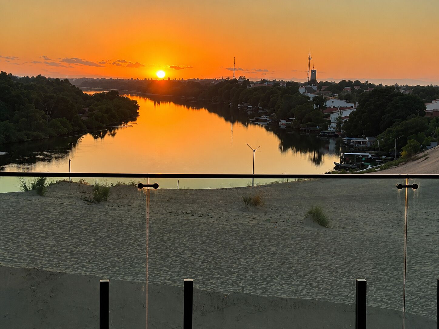 A sunset over a calm river with a bridge in the foreground and buildings in the background.