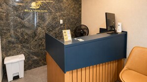 Un mostrador de recepción con pared de mármol, panel de madera, un ventilador, un cubo de basura y una silla.