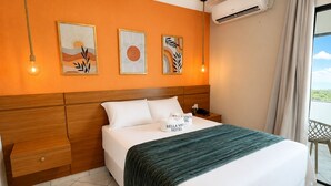 Habitación de hotel con una cama, una mesita de noche, aire acondicionado de pared y una obra de arte.
