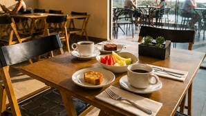 Comedor con una mesa preparada para dos personas, que incluye platos de comida, tazas de café y una planta pequeña.