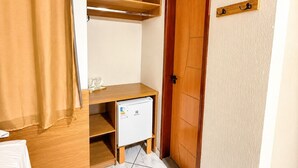 Una habitación compacta con escritorio de madera, refrigerador pequeño y un perchero en la puerta.