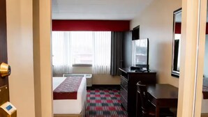 Une chambre d’hôtel avec un lit, un bureau, une chaise et une moquette à motifs.