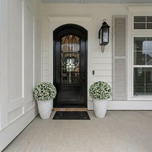 A black front door with a decorative glass panel, flanked by two white planters with green foliage, and a black lantern on the wall to the right. - THE SALTY ELK, beautiful gulf view 4 bedroom 2.5 bath home in Pass Christian, (Pass Christian)