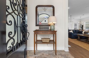 A wooden console table with a lamp, a wicker basket, and a mirror reflecting a house and flag. - THE SALTY ELK, beautiful gulf view 4 bedroom 2.5 bath home in Pass Christian, (Pass Christian)