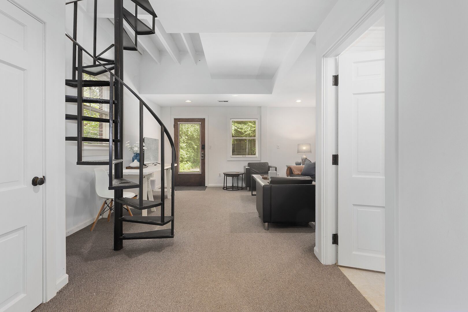 Un intérieur moderne avec un escalier en colimaçon, un coin salon avec un canapé et une table, et une porte donnant sur une autre pièce.