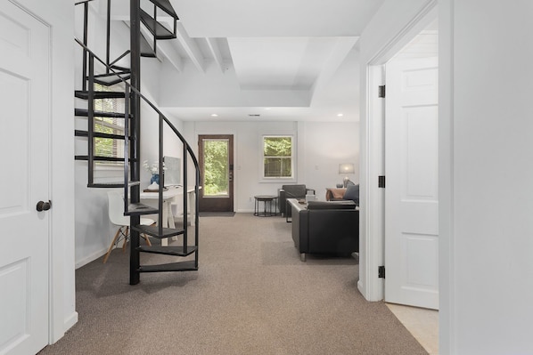 A modern interior with a spiral staircase, a seating area with a sofa and table, and a door leading to another room.