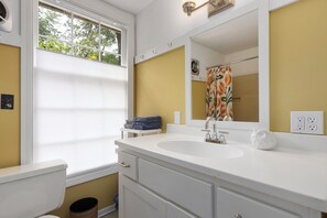 A bathroom with a white sink, a mirror, a toilet, and a window with blinds.