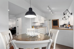 A modern kitchen with white cabinets, a dining table with white chairs, and pendant lighting.