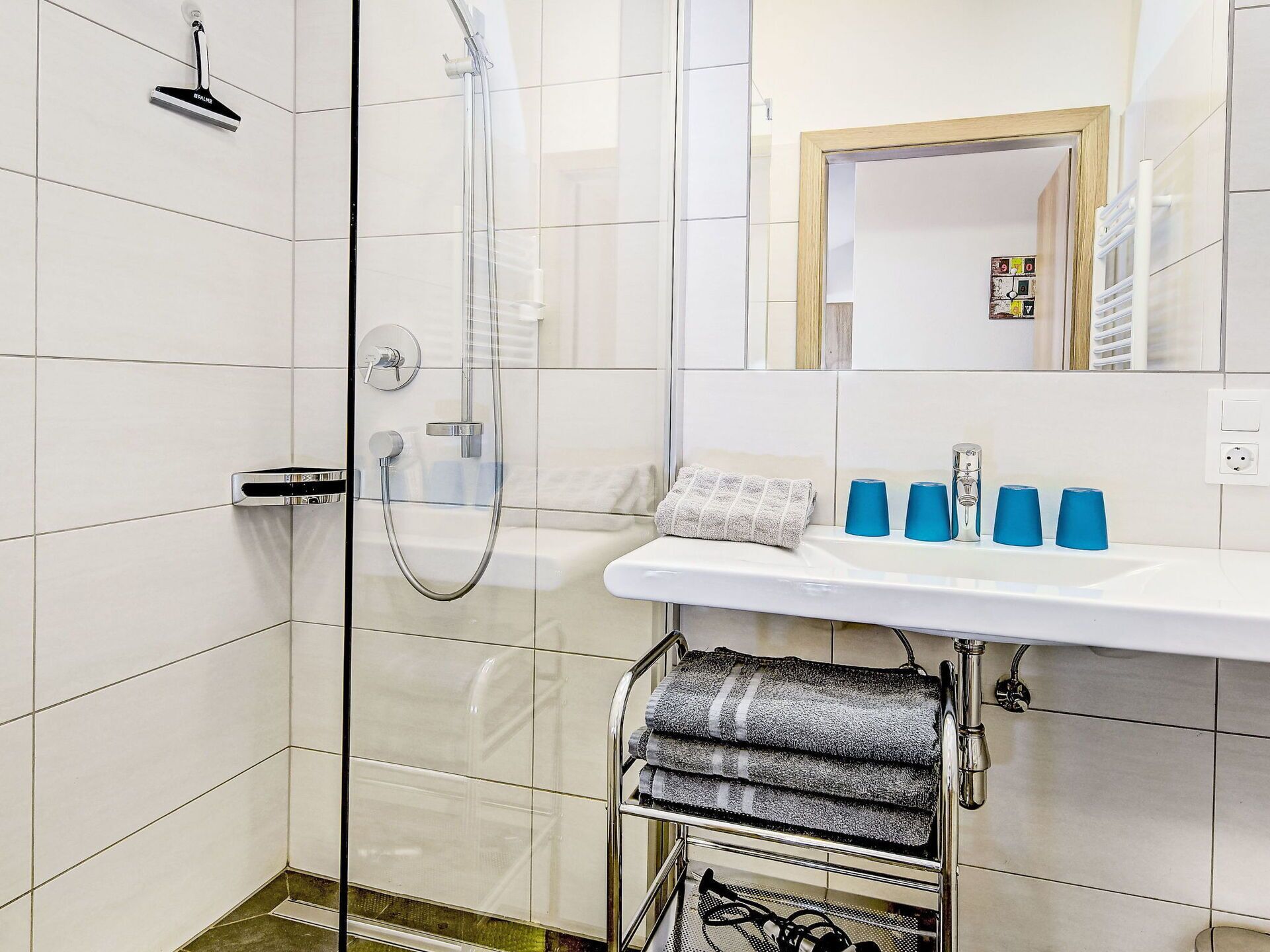 Een moderne badkamer met een douchecabine van glas, een witte wastafel met blauwe zeepdispensers en een handdoekrek.