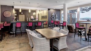 Una cocina moderna con asientos de bar, un comedor con mobiliario de mimbre y un amplio ventanal con vistas.