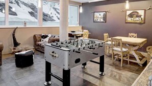 Una habitación con mesa de futbolín, sofá, mesa de comedor y sillas.