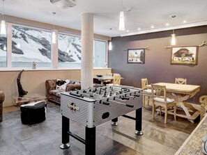 Ein Zimmer mit Tischfußball, einer Couch, einem Esstisch und Stühlen.