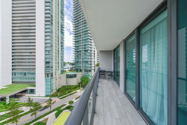 A balcony with a view of high-rise buildings, a paved area with greenery, and a clear sky. - Luxury 3BR - Rooftop Pool - One Free Parking Spot (Miami)