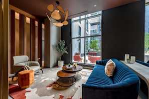 A modern lounge area with a sofa, armchair, and round coffee table. Large windows provide a view of the outside. - Modern Apt Near DC & Metro | Pool & Gym (Arlington)