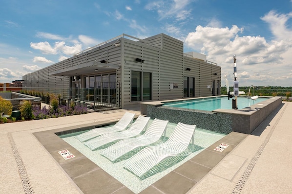 A modern building with a pool area, including lounge chairs and a hot tub. - Modern Apt Near DC & Metro | Pool & Gym (Arlington)