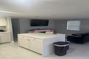 A modern kitchen with white cabinetry, a central island, and a black trash bin. - Cozy 2-bedroom house in charming Port Richey with AC (Port Richey)