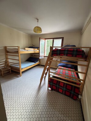 Een studentenkamer met stapelbedden, een raam met uitzicht op bomen, en een plafondventilator.