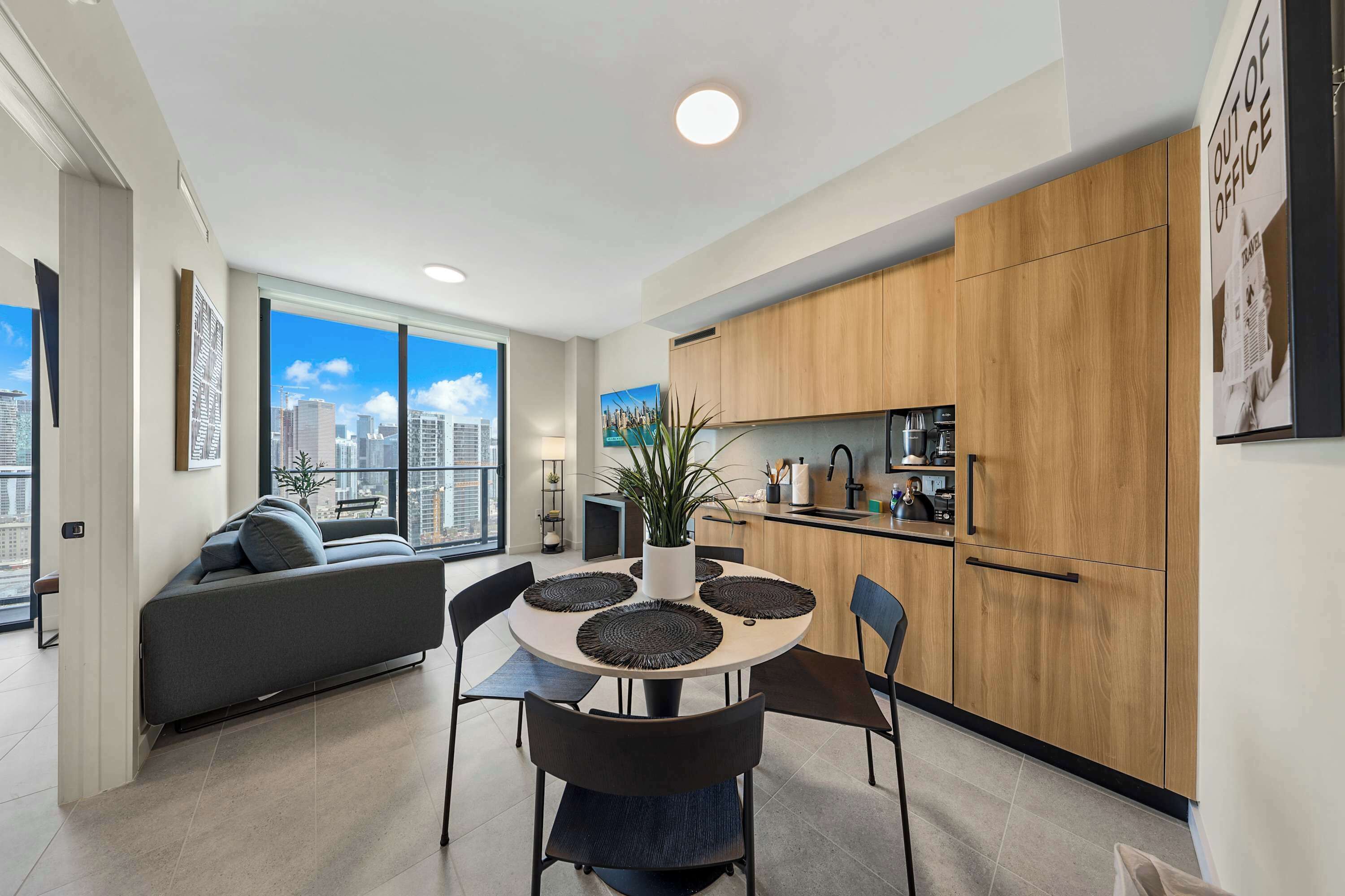 A modern apartment with a dining area, kitchen, and a large window with a city view.