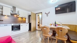 Een moderne keuken met witte kastjes, een ingebouwde oven en een eethoek met houten stoelen en een tafel gedekt voor twee personen.