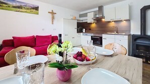 Een moderne keuken met witte kasten, een zwarte kookplaat en een houten eettafel met een roze vaas en glazen.