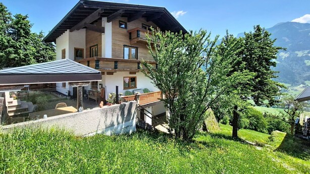 Een meerlaags gebouw met een balkon, een glazen uitbouw en uitzicht op een bergachtig landschap.