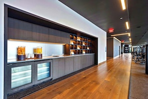 A modern reception desk with a glass partition, wooden flooring, and a hallway leading to a gym area. - New 3BR - Rooftop Pool - Steps to Fan Fest (Miami)