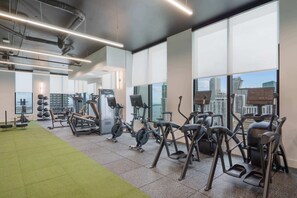 Ein Fitnessstudio mit Trainingsgeräten, großen Fenstern und Blick auf die Skyline.