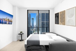 Ein modernes Hotelzimmer mit großem Fenster, einem Bett, einem kleinen Tisch mit Pflanze und Kunstwerken an den Wänden.