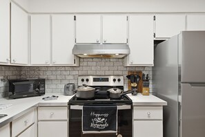 Une cuisine avec des meubles blancs, une cuisinière en acier inoxydable, un four à micro-ondes et un réfrigérateur.