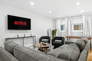 A modern living room with a flat-screen TV, grey sofas, a coffee table, and a futon.