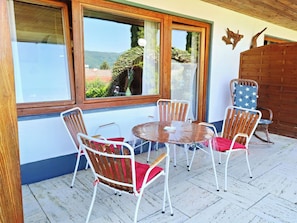 Eine Terrasse mit einem runden Tisch und vier Stühlen, großen Fenstern und einer Holzverkleidung.