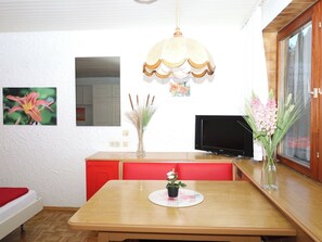 Ein Essbereich mit Holztisch, roten Stühlen, einem Fernseher und dekorativen Vasen.