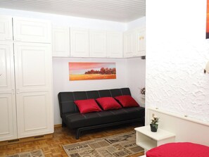Ein Zimmer mit einer schwarzen Couch, roten Kissen, einem Gemälde, weißen Schränken und einem gemusterten Teppich.