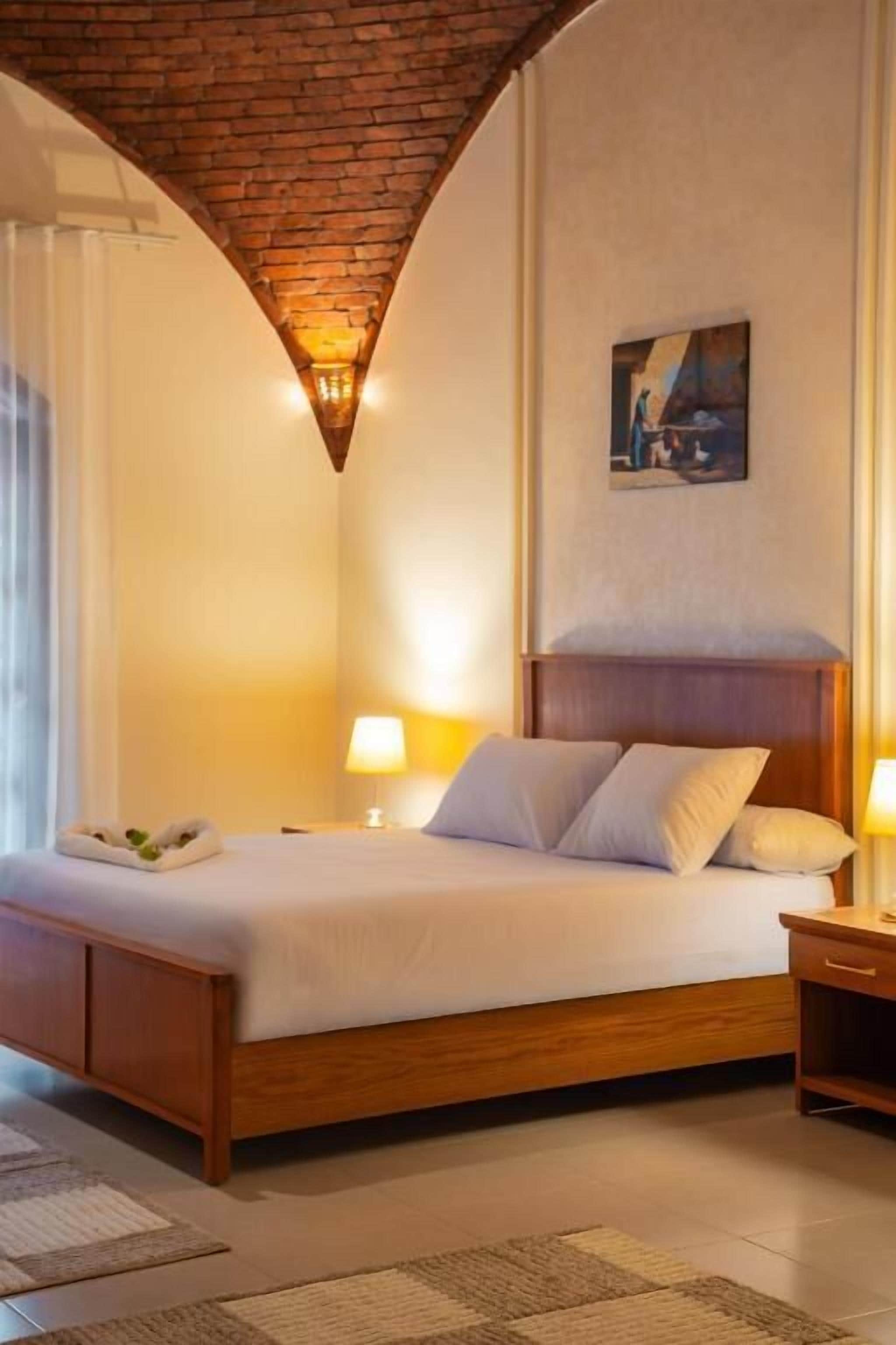 A hotel room with a wooden bed, a painting on the wall, and a brick ceiling.