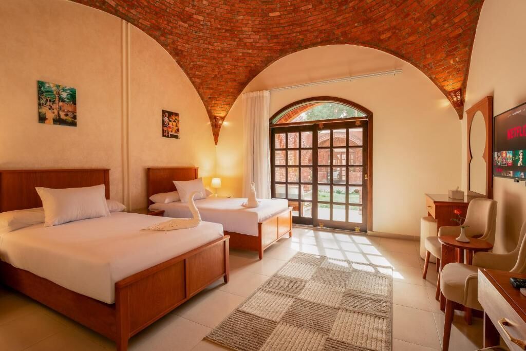 Una camera d'albergo con soffitto in mattoni, un'ampia finestra ad arco, un letto, una scrivania e una televisione.