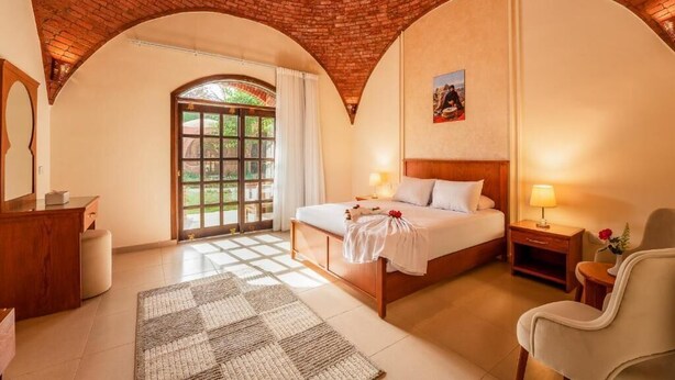 Habitación de hotel con techo de ladrillo, una cama grande, un escritorio, una silla y un ventanal con cortinas.