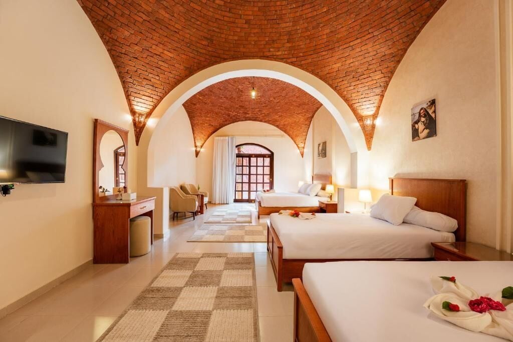 Ein Hotelzimmer mit Backstein-Decke, zwei Betten, einem Fernseher, einem Schreibtisch und einem Badezimmer.