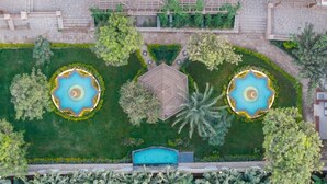 Vista aérea de un área ajardinada con dos fuentes circulares, una estructura central y una piscina.