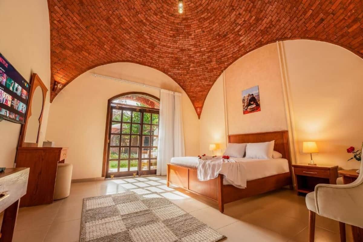 Un dormitorio con techo de ladrillo, una cama, un escritorio y vistas a zonas verdes.