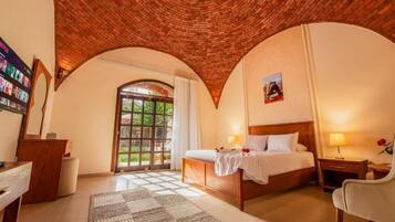 Un dormitorio con techo de ladrillo, una cama, un escritorio y vistas a zonas verdes.