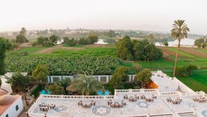 A rooftop terrace with outdoor seating and a view of agricultural fields and a body of water. - Opal Legacy Luxor (Luxor)