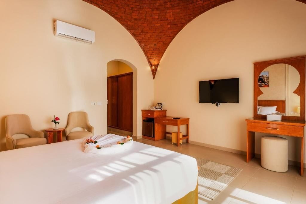A hotel room with a bed, two chairs, a desk, a TV, and a mirror.