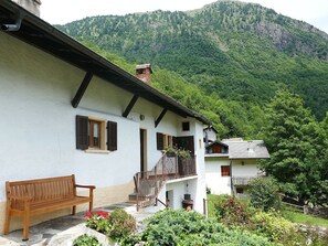 Ein weißes Gebäude mit Holzbank, Balkon und Bergblick.
