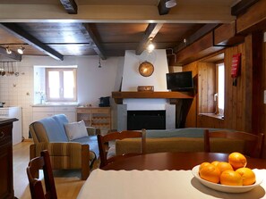 Ein gemütliches Wohnzimmer mit Kamin, einem Esstisch mit einer Orangenschale und einem Fernseher.