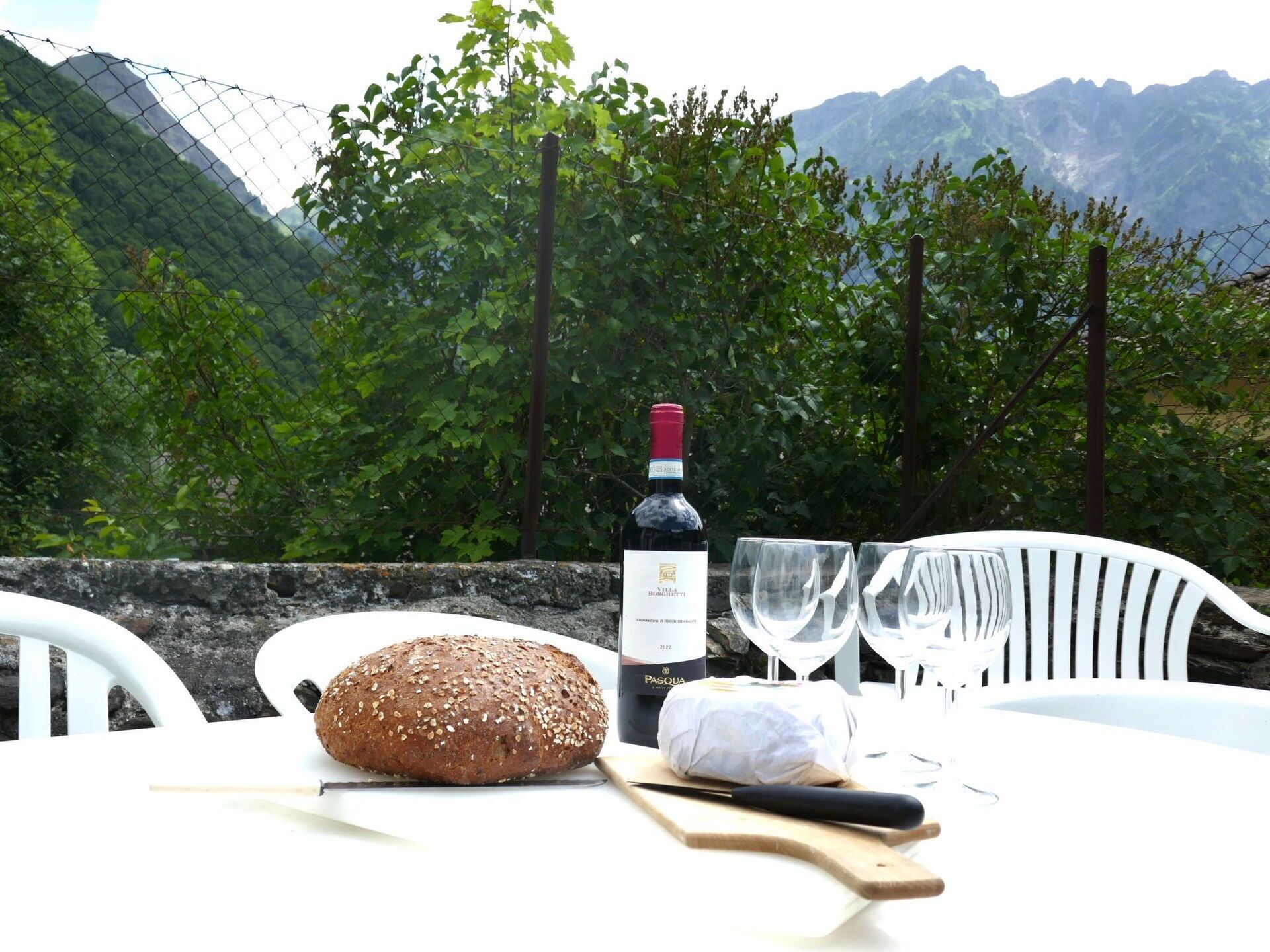 Een tafel met een brood, een fles wijn, twee glazen en een mes op een snijplank.