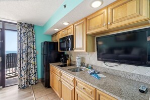 A kitchen with wooden cabinets, a black refrigerator, a microwave, a sink, and a flat-screen TV. - Beach Cove Resort 1014 - Oceanfront Condo with Direct Beach Access (North Myrtle Beach)