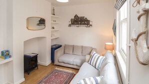 A cozy living room with a sofa, a small table, a fireplace, and decorative wall art. - Pixie Cottage (Weymouth)