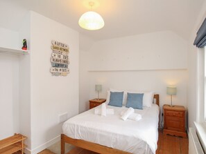 Ein Schlafzimmer mit einem Bett, zwei Nachttischen, einer Wandlampe, einem Regal mit einem dekorativen Schild und einem Fenster mit Vorhängen.
